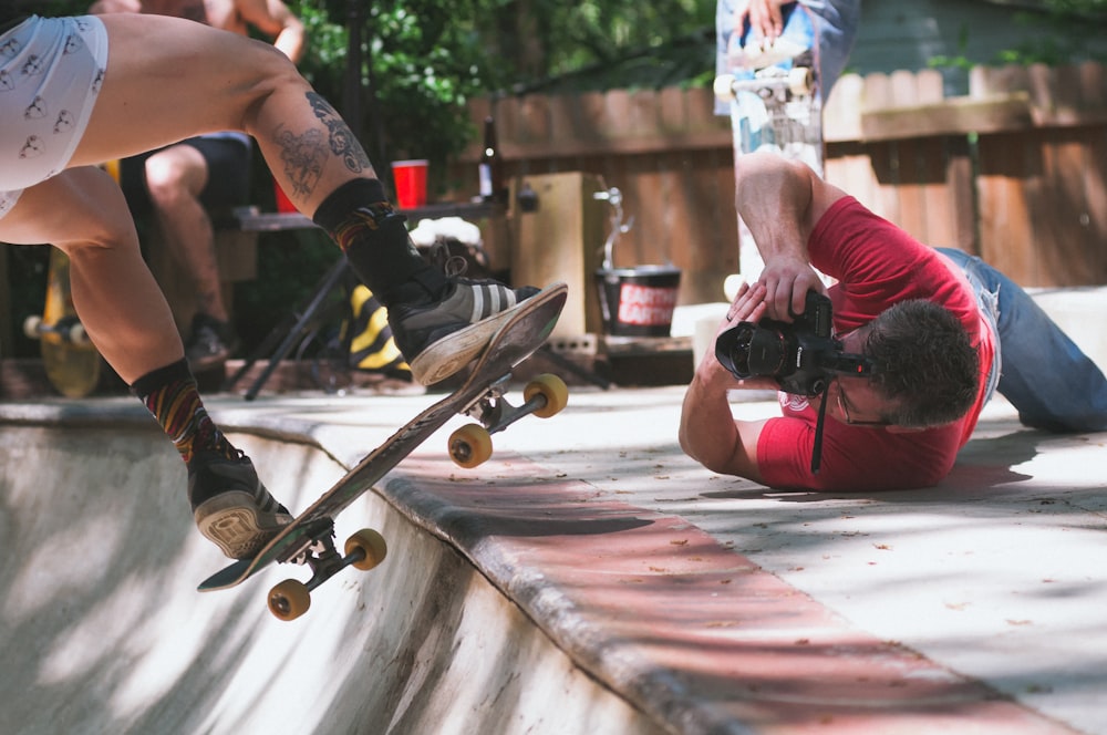 man lying on floor while taking picture of person doing skate trick on ramp