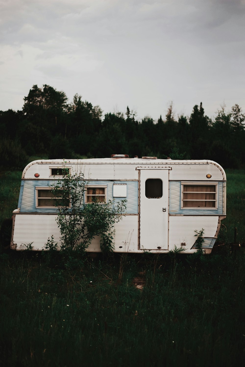 white RV trailer on grass field near trees under cloudy sky