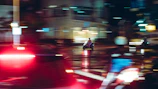 An afsar model speeding through a city street at dusk, city lights reflecting off its sleek black frame.