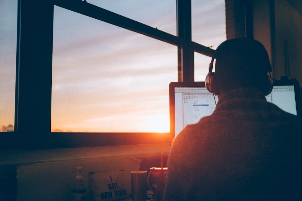 Man wearing headphones at desk with window view of sunset in background