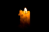 A flickering candle casting warm light in a sacred, darkened space.