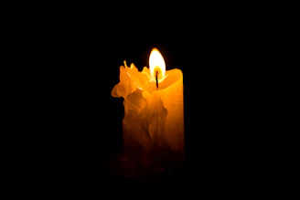 A flickering candle casting warm light in a sacred, darkened space.