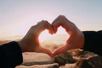 A soft-focus photo of a hand gently holding another on a sandy beach at sunset.