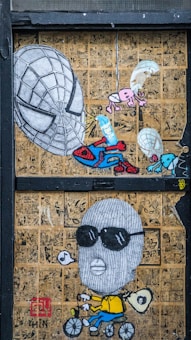 The artwork features a collage of comic book pages in the background with a prominent illustration of a large Spiderman-like mask, alongside a cartoonish figure wearing sunglasses and a balaclava, riding a bicycle and blowing a bubble. Smaller elements include parachuting creatures and an abstract figure holding a pencil.
