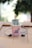 A popsicle is placed upright in a pink paper cup labeled 'POP EYES' with a playful design featuring cartoon eyes. The popsicle is green and has a frosty texture. Surrounding the cup is a pair of black earphones, and everything rests on a wooden surface, creating a casual and laid-back atmosphere.