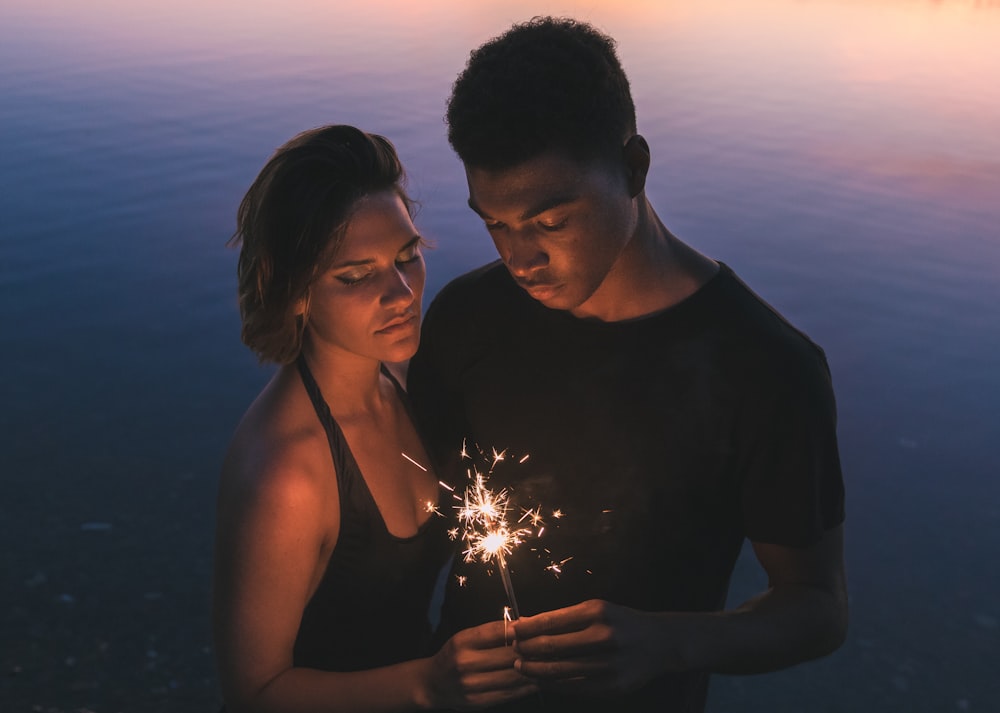 man and woman holding sparkler near body of water