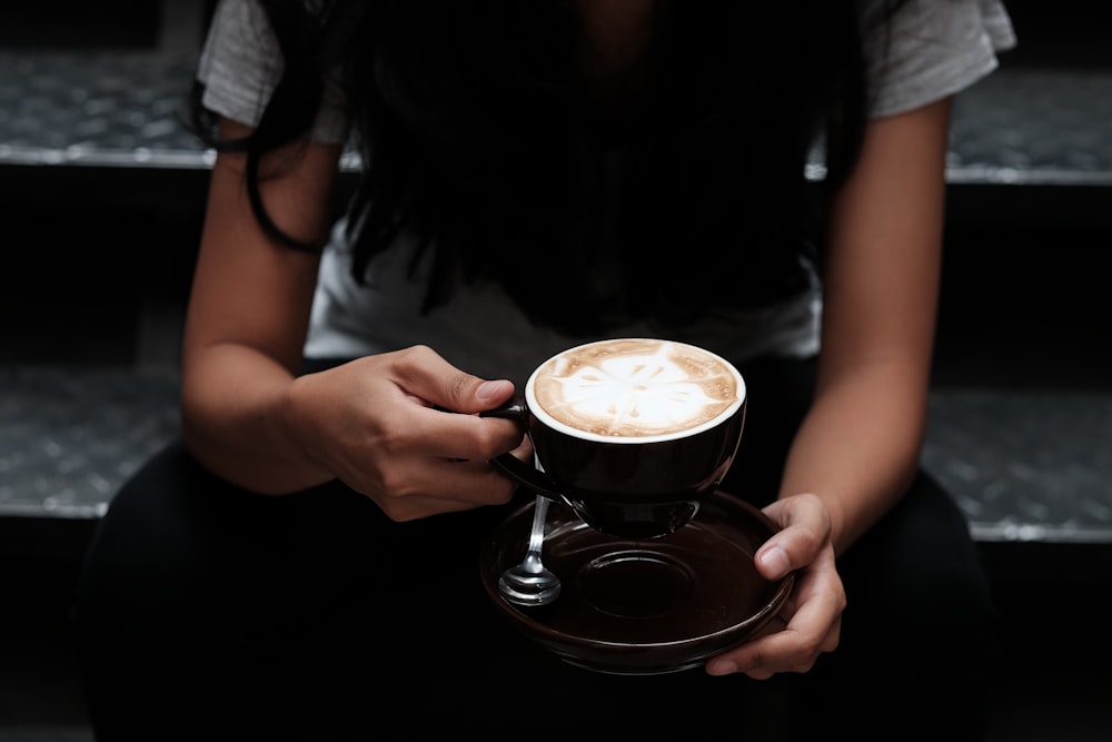 woman carrying cup of coffee with saucer while sitting on gray stairs