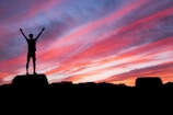 silhouette of man standing on high ground under red and blue skies