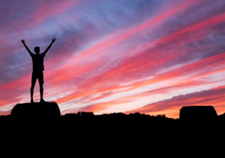 silhouette of man standing on high ground under red and blue skies