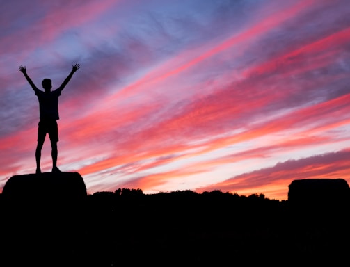 silhouette of man standing on high ground under red and blue skies