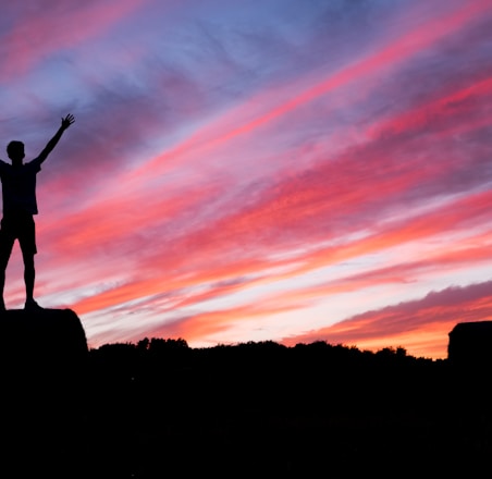 silhouette of man standing on high ground under red and blue skies