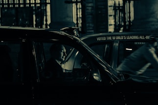 A friendly taxi driver helping a passenger with luggage at night in the UK.