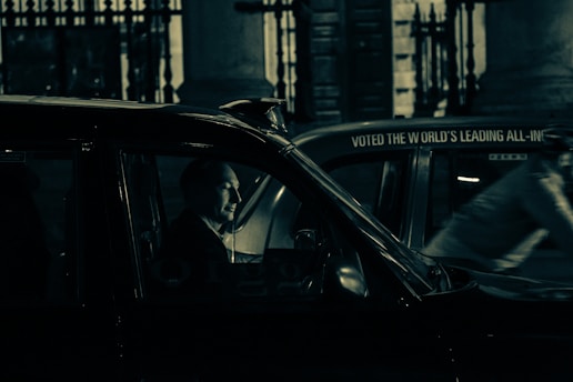 A friendly taxi driver opening the car door for a passenger at night in a UK city.