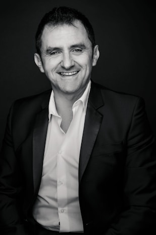 A friendly news anchor smiling warmly in front of a modern digital news set.