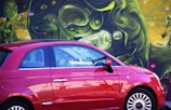 A compact car parked by a colorful Tucson street mural showcasing local culture.