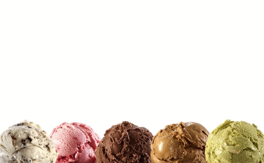 Five different scoops of ice cream are neatly aligned, each varying in color, including shades of brown, pink, green, and vanilla with chocolate chips.