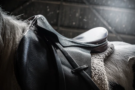 Close-up of premium leather horse saddle with detailed stitching in a rustic stable setting.