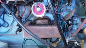 A complex arrangement of electrical components including wires of various colors, a transformer, resistors, and a circular pink gauge. The setup appears aged and dusty, with some rust visible on the metallic surfaces.