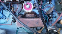 A complex arrangement of electrical components including wires of various colors, a transformer, resistors, and a circular pink gauge. The setup appears aged and dusty, with some rust visible on the metallic surfaces.