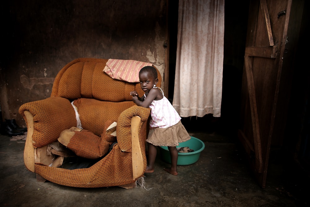 girl standing near brown fabric sofa chair inside room