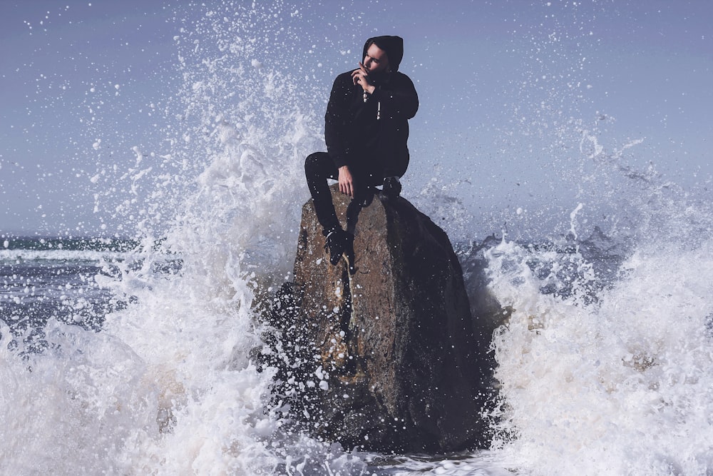 水の真ん中の岩の上に座る黒いジャケットの男