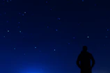 A silhouette of a lone traveler gazing at distant stars framed by cosmic dust.
