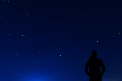 A silhouette of a lone traveler gazing at distant stars framed by cosmic dust.