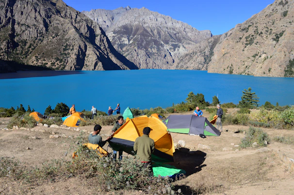 A family setting up a colorful tent beside a gently flowing river under a clear blue sky