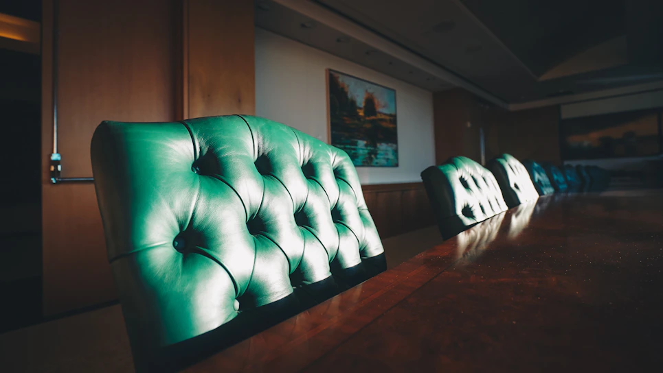 A refined executive boardroom bathed in warm, natural light with sleek leather chairs around a polished wooden table.