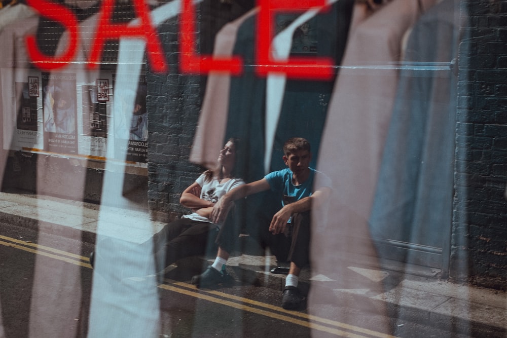 two people sitting on sidewalk