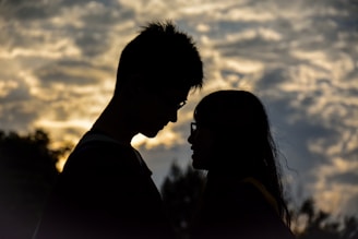 Silhouettes of a man and woman facing each other with a dramatic cloud-filled sky in the background, conveying a sense of intimacy and connection.