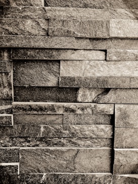 A textured wall made of rectangular stone slabs arranged in a staggered pattern. The stones vary in shade, creating a rustic and natural look.