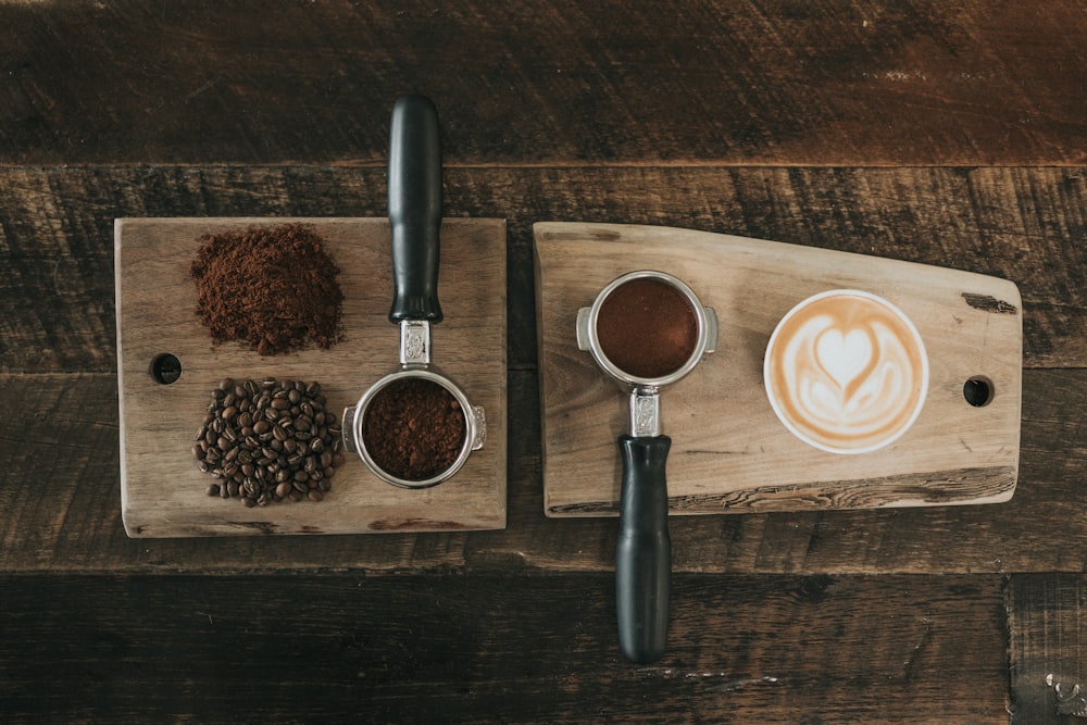 Grãos de café ao lado do pó de café e uma xícara de café com leite estilo latte, sob uma placa de madeira marrom.