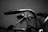 Close-up shot of a black leather riding glove gripping a motorcycle handlebar, with subtle matte black and white tones.