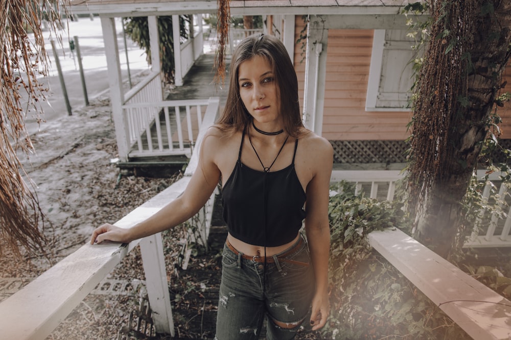 woman in black spaghetti strap top and blue denim jeans standing on white wooden stairs during