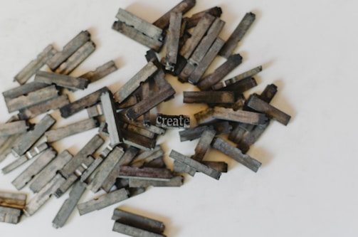 A collection of numerous metallic type blocks, typically used in traditional printing, scattered on a light background. One block in the center is upright and visible, displaying the word 'Create'. The blocks exhibit various shades of gray and black, with a worn-out, aged appearance.