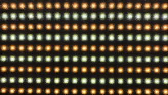 A grid pattern of small LED lights arranged in rows, alternating in color between warmer orange and cooler white tones. The lights are set against a dark background, emphasizing their glow.