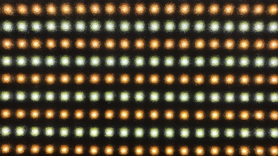 A grid pattern of small LED lights arranged in rows, alternating in color between warmer orange and cooler white tones. The lights are set against a dark background, emphasizing their glow.
