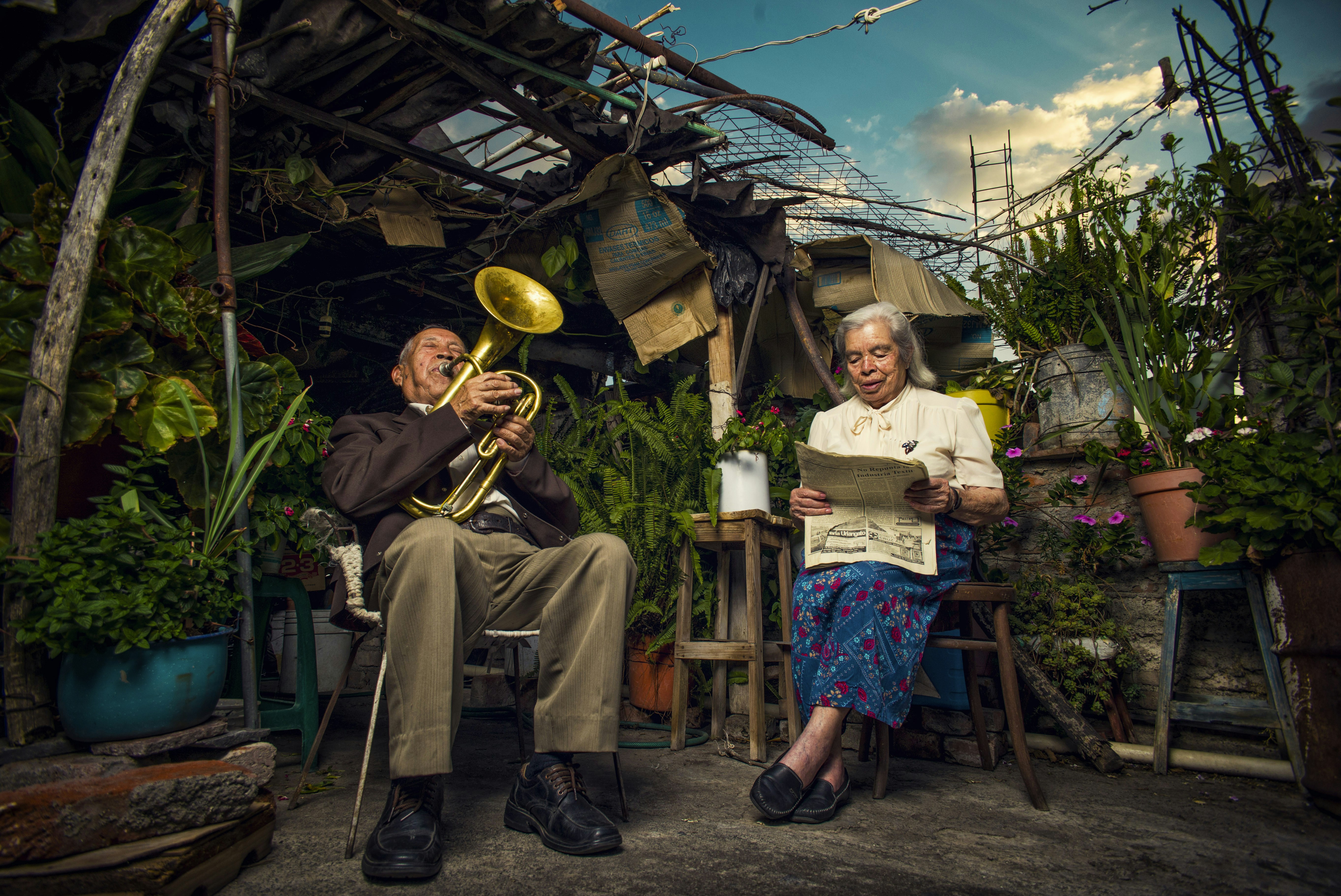 An old woman reads the paper while her husband plays a horn in Yuriria amidst patio plants