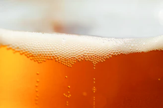 Close-up of a frosty glass of amber beer with bubbles rising, set on a rustic wooden table.