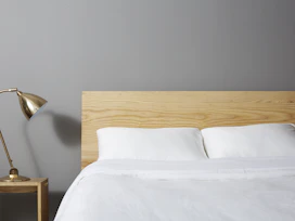 Modern bedroom with soft white linens and a minimalist wooden headboard.