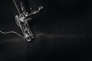 photo of gray sewing machine foot lock with thread on black cloth