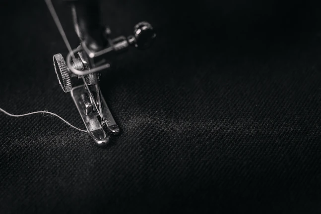 Close-up of a tailor stitching a sleek black sports hoodie with gold thread.