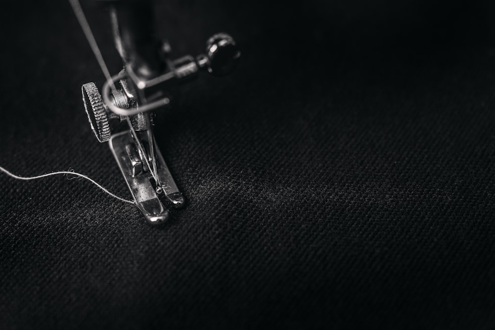 Foto di blocco del piede della macchina da cucire grigia con filo su panno nero