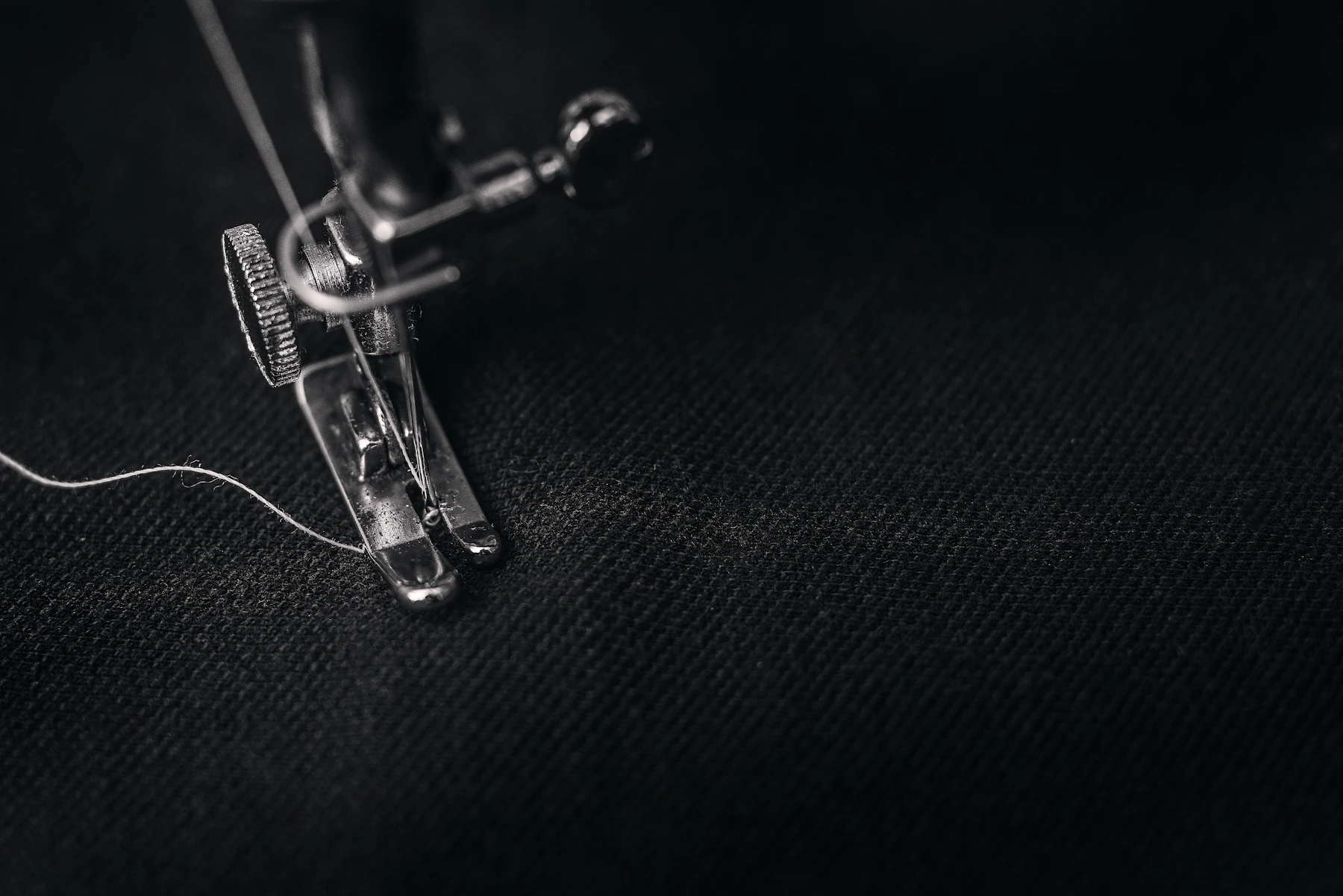 Close view of a sewing foot stitching dark cloth