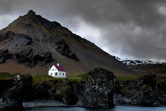 white house near brown mountain and body of water in Westfjords Region Iceland