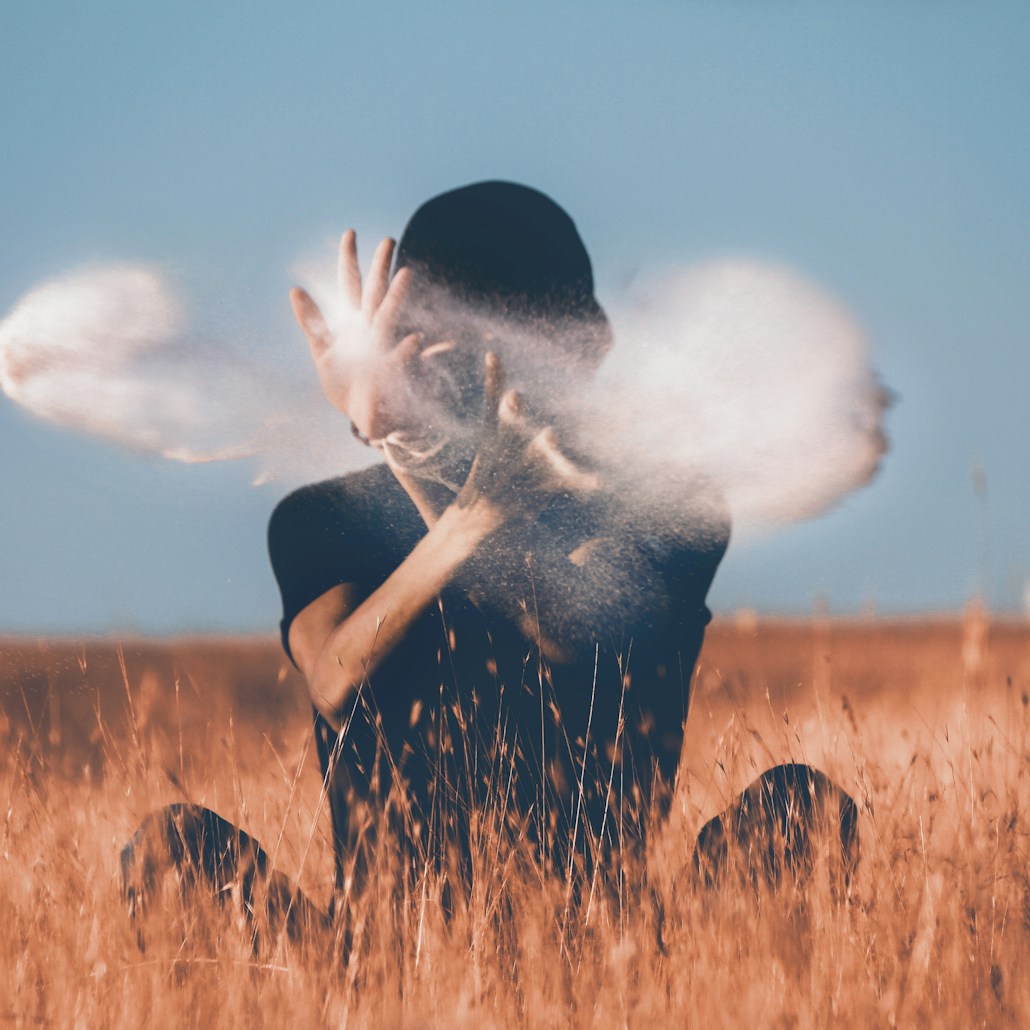 man sitting on brown grass field playing with smoke