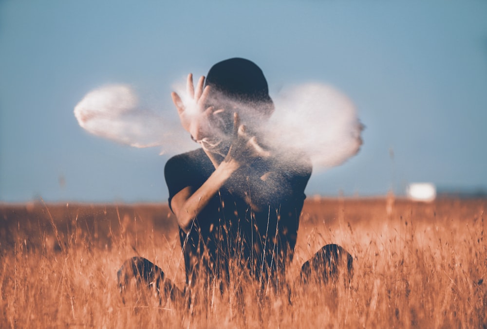 man sitting on brown grass field playing with smoke