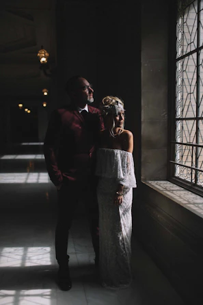 An intimate moment of a groom adjusting his tie, framed by delicate window light.