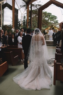 A groom wiping a tear as he watches his bride walk down the aisle in a sunlit chapel.